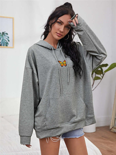 Model wearing a loose grey hooded sweatshirt with butterfly embroidery, perfect for casual style.