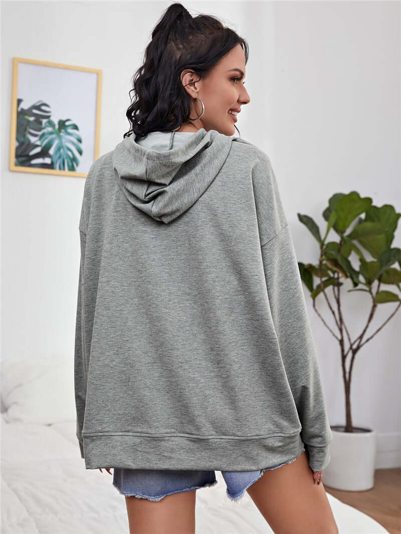 Back view of a woman in a loose printed drop-shoulder hooded sweatshirt in gray, styled with casual shorts.