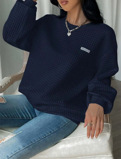 Navy blue drop shoulder sweatshirt with letter patch detail, styled with ripped jeans and necklace.