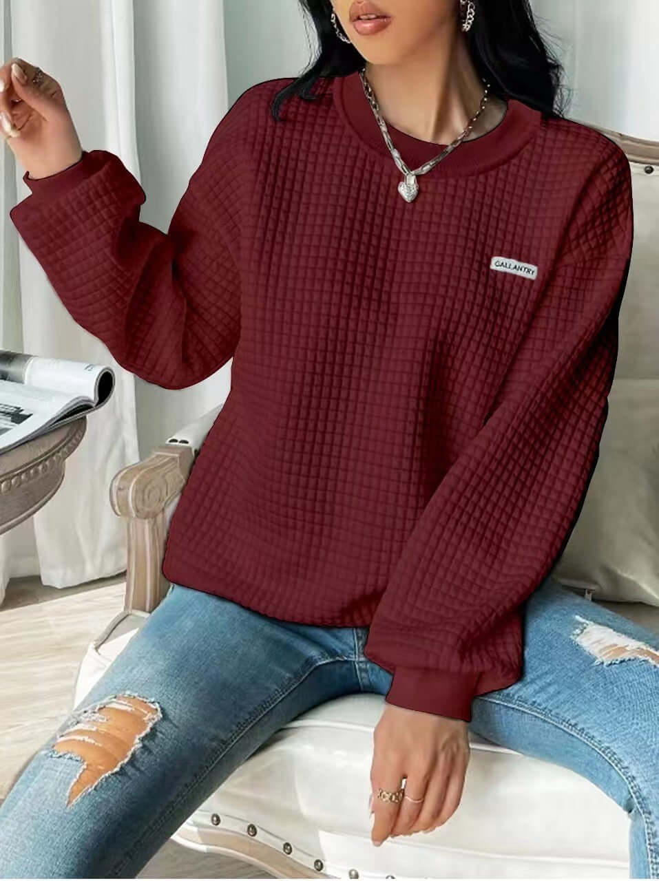 Female model wearing a wine red drop shoulder sweatshirt with letter patch detail and long sleeves.