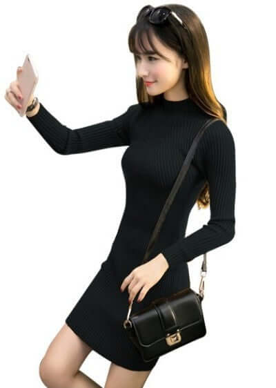 Fashionable woman in a black half high neck knit dress with long sleeves, holding a smartphone and a stylish handbag.