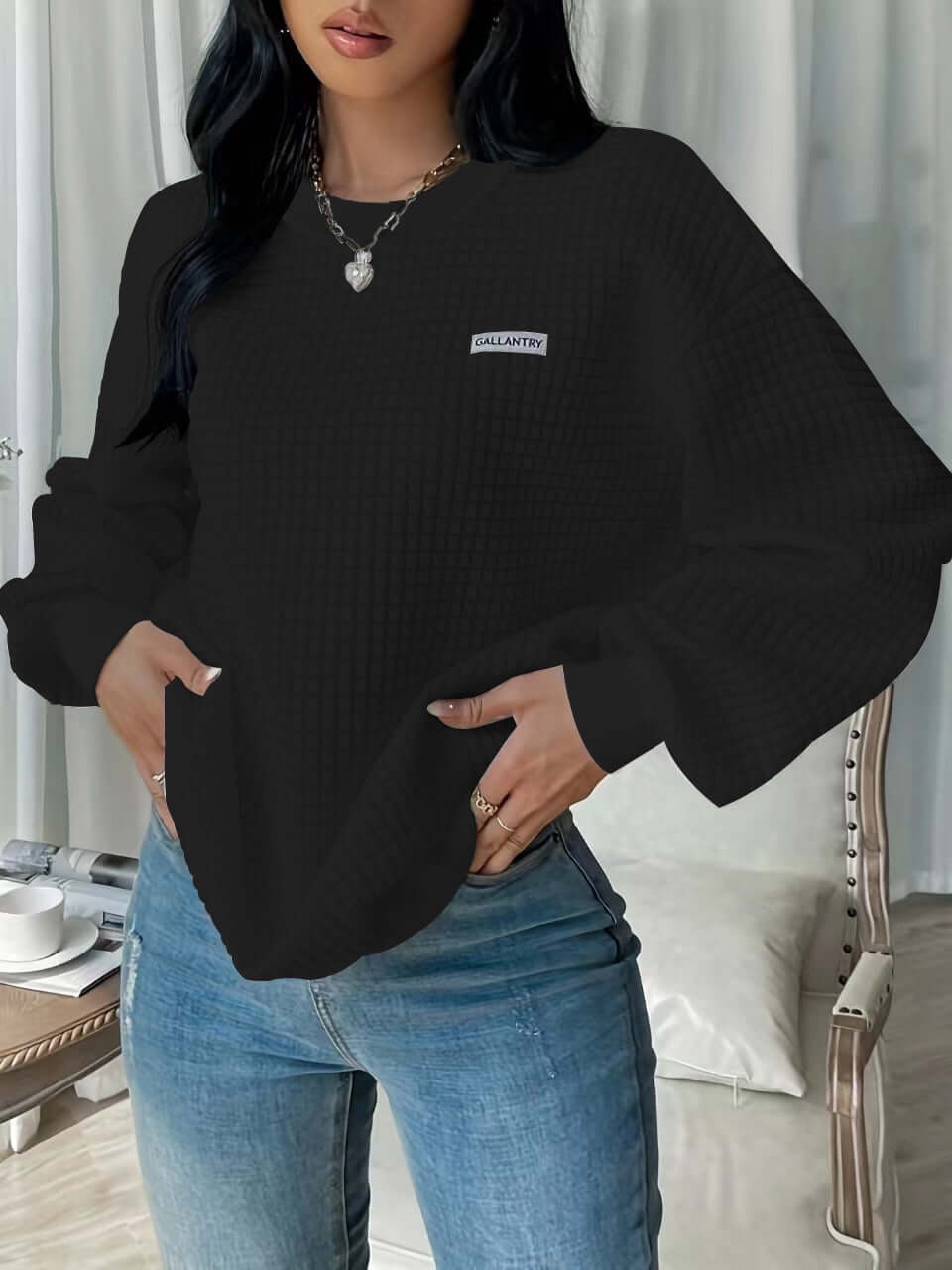 Black drop shoulder sweatshirt with letter patch detail, styled with jeans and a chic backdrop.