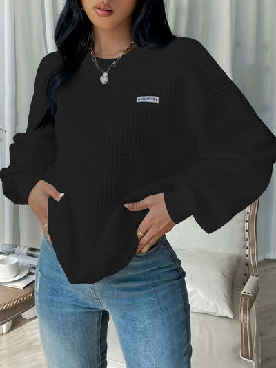Black drop shoulder sweatshirt with letter patch detail, styled with jeans and a chic backdrop.