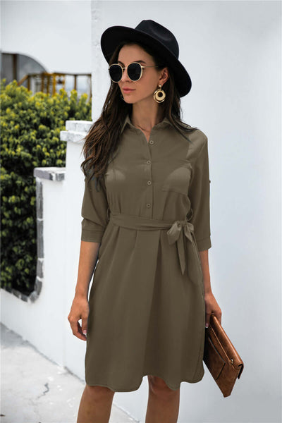 Solid color button lapel mid-sleeve shirt dress in olive green, styled with a black hat and sunglasses.