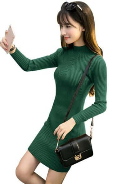 Model in a green ribbed knit half high neck dress with long sleeves, holding a phone and a handbag.