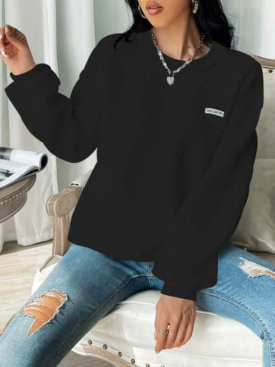 Black drop shoulder sweatshirt with letter patch detail, long sleeves, styled for women, casual wear.