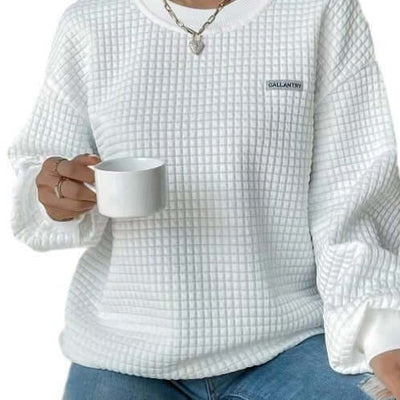Female model wearing a white drop shoulder sweatshirt with a textured pattern, holding a coffee cup.