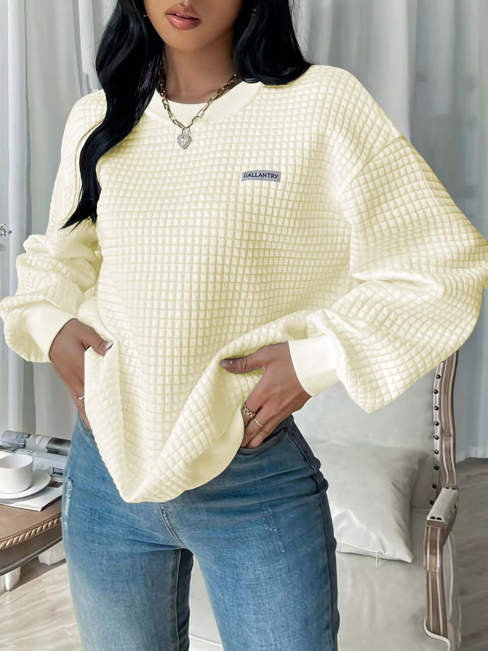 Woman wearing a cream drop shoulder sweatshirt with textured fabric, styled with blue jeans.