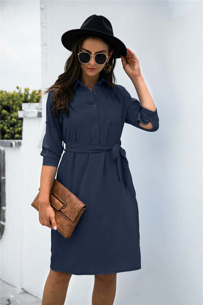 Solid color button lapel shirt dress with mid-sleeves and belt, paired with a stylish hat and oversized sunglasses.